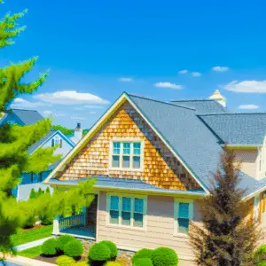 A suburban house with a gabled roof, wood siding, and manicured shrubs, photographed on a clear sunny day.